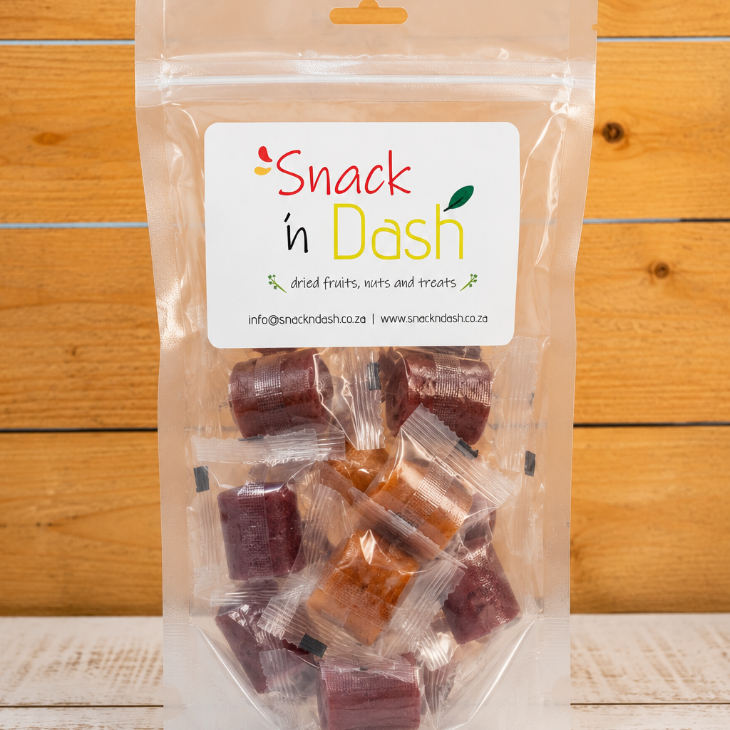 A clear plastic stand-up pouch of Snack in Dash dried fruits, nuts, and treats, containing several individually wrapped reddish-brown and purple candy pieces, set against a rustic wooden background.