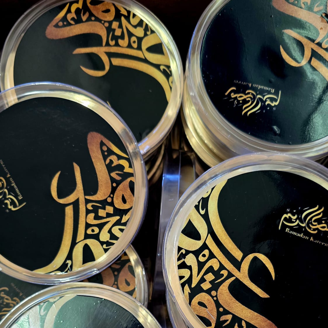 Round containers with gold Arabic calligraphy on black background